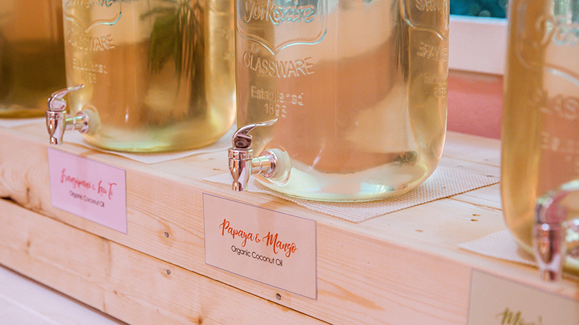 Two large glass jars with taps holding Mailelani scented coconut oil for refills