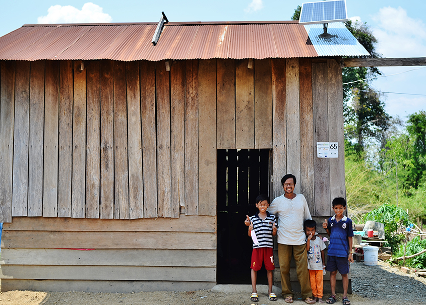 A family in front of a rural house in a remote location in Cambodia who uses Okra Solar Mesh-Grids