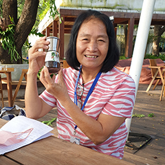 Patthama Wongnopparat, owner of Wongnopparat Pepper Farm sitting at a wooden table, in a garden, holding a glass pot filled with “Chanthaburi Pepper” with an integrated pepper mill