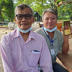 Prasroed Chuntrakun, Vice-Chairman of the Sakaeo Mango Community, sitting on a bench in a garden with a GI producer of “Sa Kaeo Nam Dok Mai Mango”