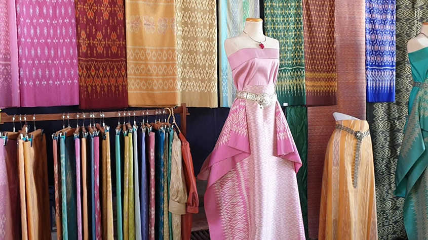 Colorful silk scarfs display, with in front of it, a shop mannequin draped in a pink piece of silk fashioned as a dress