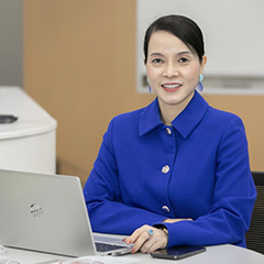 Ms. Bùi Kim Thùy, VinFast Deputy CEO, sitting in front of a laptop computer, wearing a blue jacket and matching blue earrings