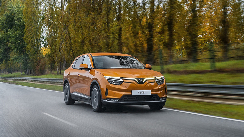 An electric VinFast VF8 orange model driving along a tree-lined road