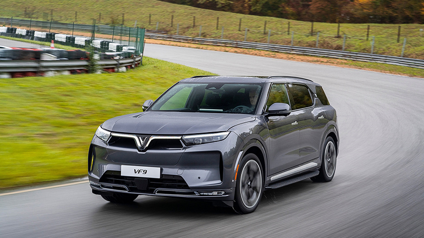 An electric VinFast VF9 grey model driving along a country road