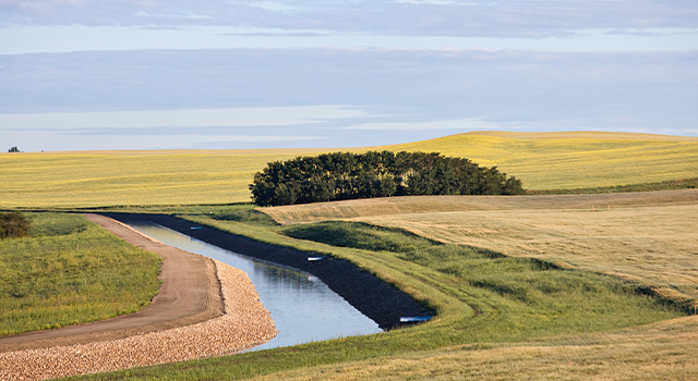 A man made irrigation canal on the prairie. Drainage ditch or agricultural irrigation canal in Alberta, Canada. Water issues and agriculture go hand in hand. This waterway is fed by the Bow River in Southwest Calgary and moves water to the rolling fields east of the city limits