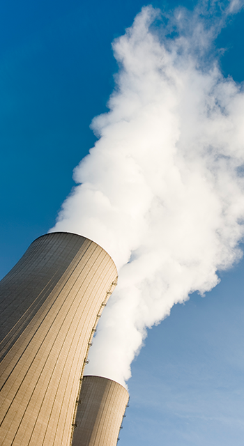 Tilt shot of Two steaming cooling towers against blue sky. Exposure with extreme wide-angle lens with tilt perspective.