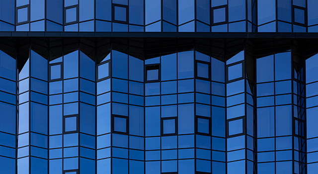 A fragment of the mirrored facade of a building with small square windows. Glazing of the facade with blue glass. Architectural background