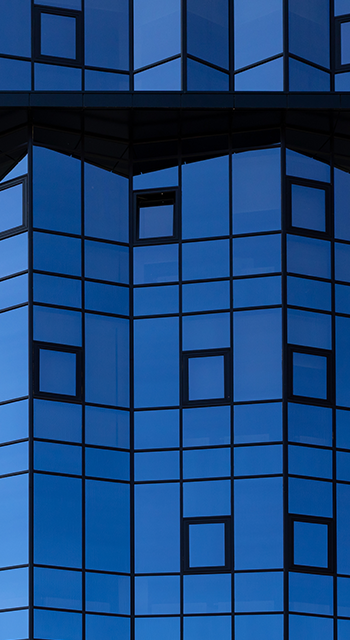 A fragment of the mirrored facade of a building with small square windows. Glazing of the facade with blue glass. Architectural background