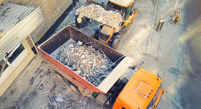 Bulldozer loader uploading waste and debris into dump truck at construction site.