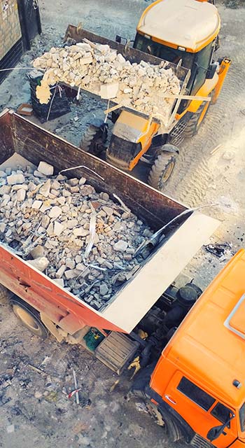 Bulldozer loader uploading waste and debris into dump truck at construction site.