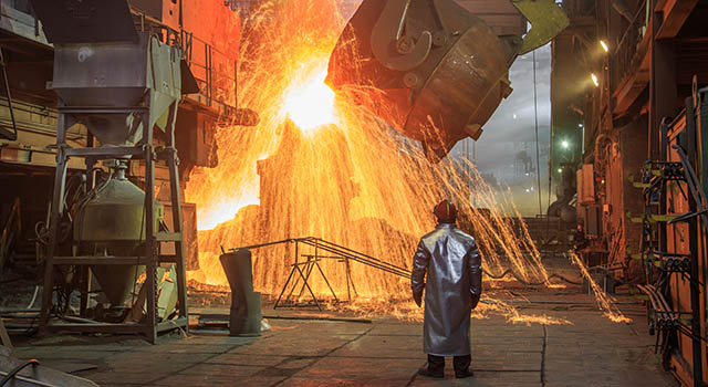 Hot steel pouring from big casting ladle into a mold in an iron foundry. Sparks, flame and smoke on the background. Factory worker controls the process.