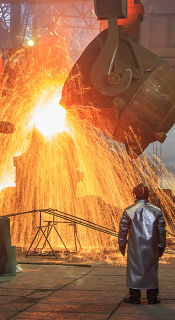 Hot steel pouring from big casting ladle into a mold in an iron foundry. Sparks, flame and smoke on the background. Factory worker controls the process.