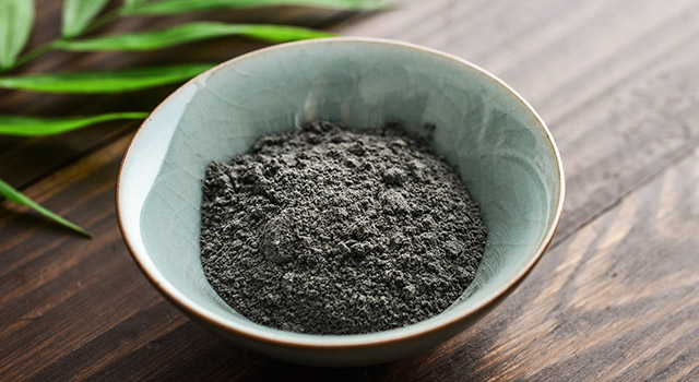 Black cosmetic clay in coconut bowl on wooden background closeup