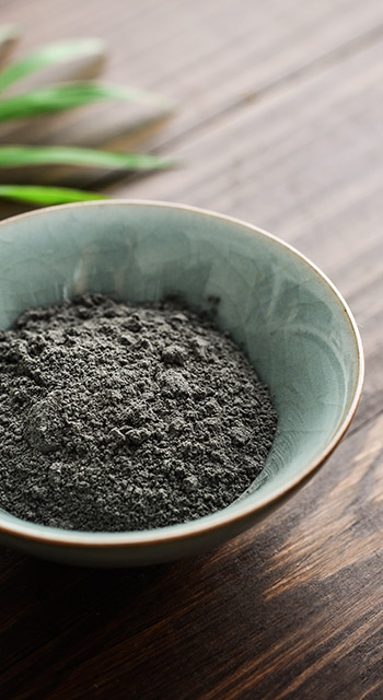 Black cosmetic clay in coconut bowl on wooden background closeup