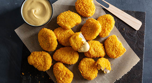 Tasty appetizing crispy chicken nuggets served on wooden board with mustard on dark background.