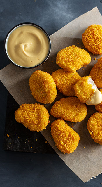 Tasty appetizing crispy chicken nuggets served on wooden board with mustard on dark background.