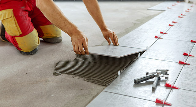 Ceramic Tiles. Tiler placing ceramic wall tile in position over adhesive with lash tile leveling system 