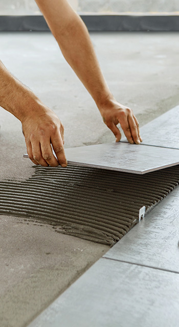 Ceramic Tiles. Tiler placing ceramic wall tile in position over adhesive with lash tile leveling system 