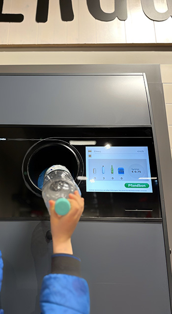 Little boy putting plastic bottles to the automatic recycling machine that is able to dispense refunds